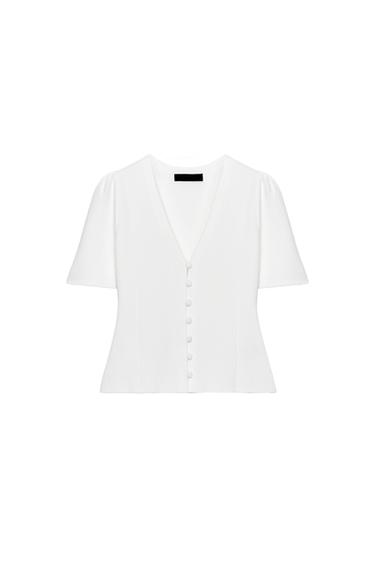 Front view of a white knitted jacket with a V-neck, wide short sleeves, and a front fastening with matching buttons.