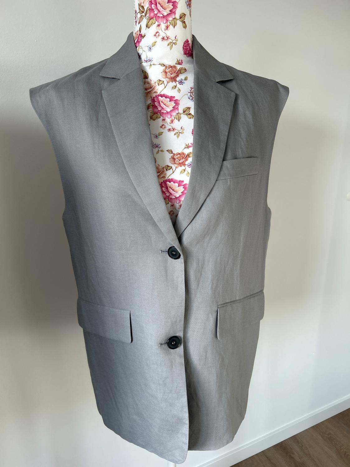 Grey sleeveless waistcoat on a mannequin with a floral print, white background, and light wooden floor.