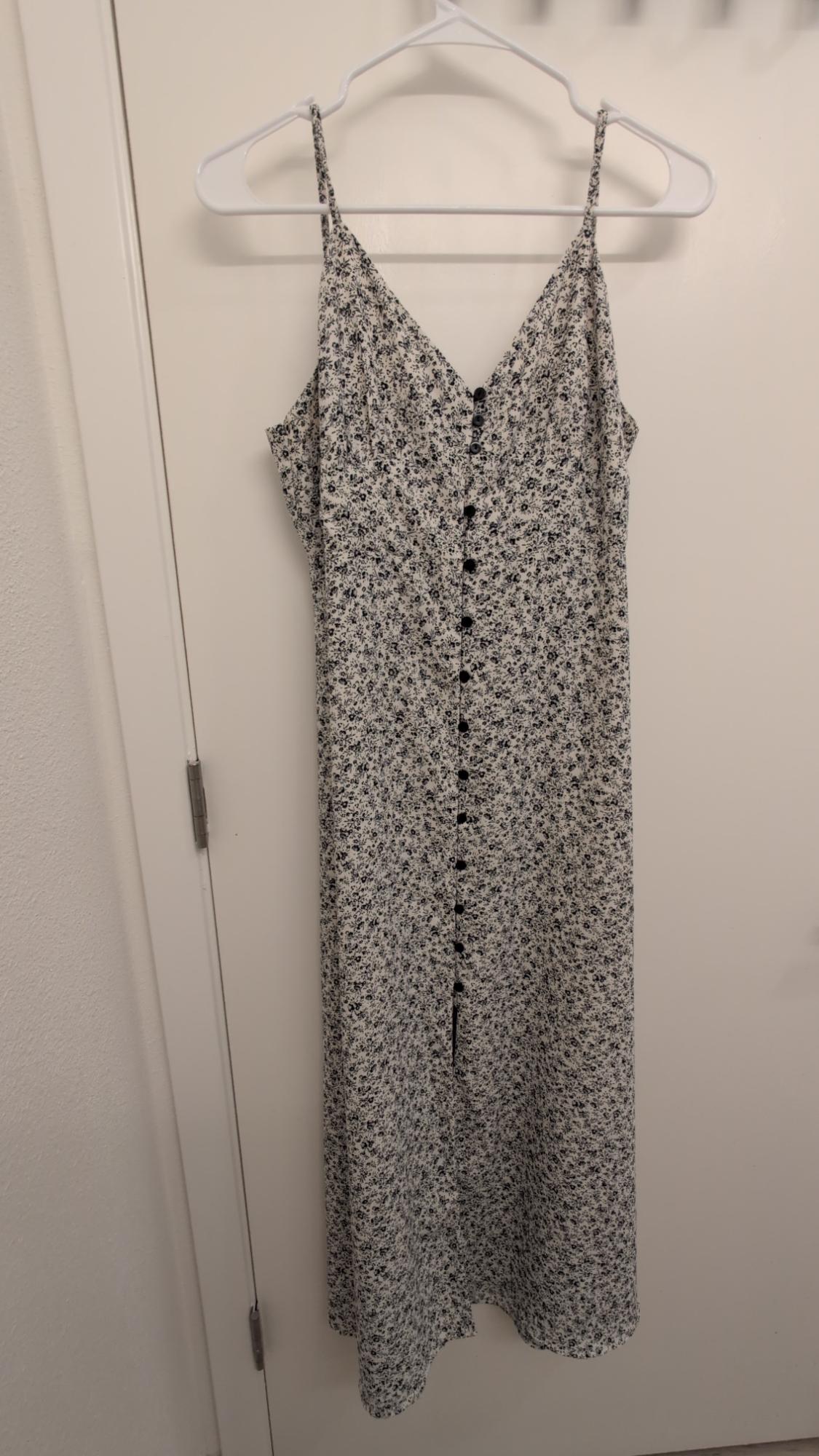 Strappy maxi dress with black and white floral print, hanging on a white hanger over a white door.