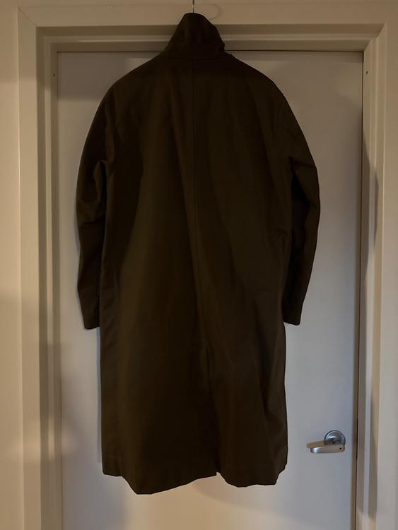 Dark long coat hanging on a white door, viewed from behind. The light creates soft shadows on the wall and the coat.