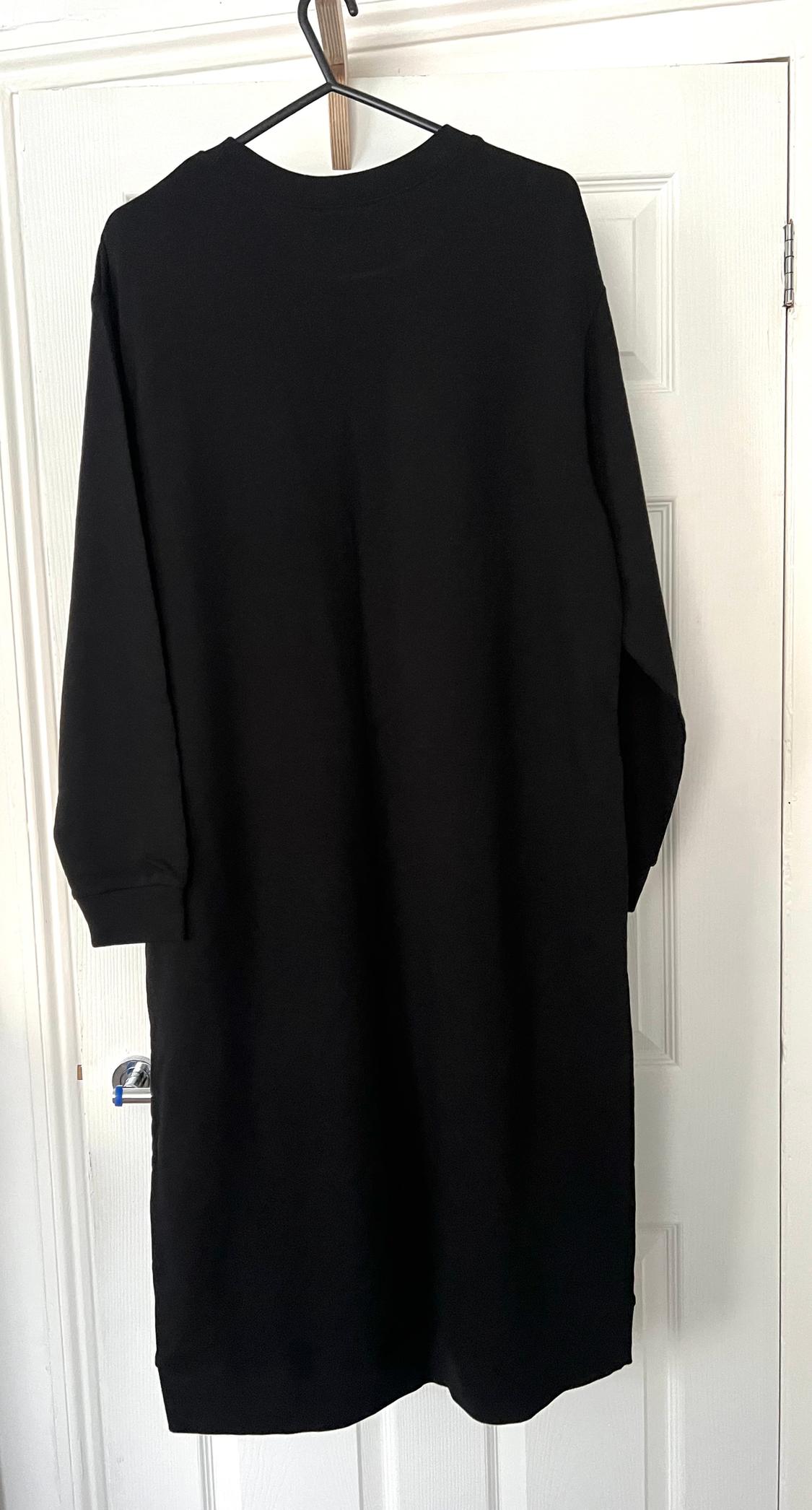 Black long-sleeved dress hanging on a hanger over a white door.