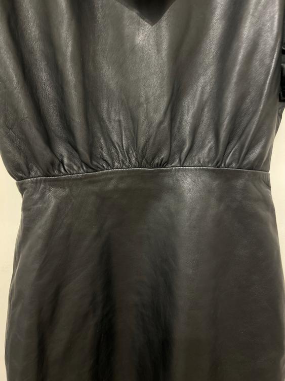 Close-up of a black leather dress with ruching at the waist, showing soft texture and a glossy finish.