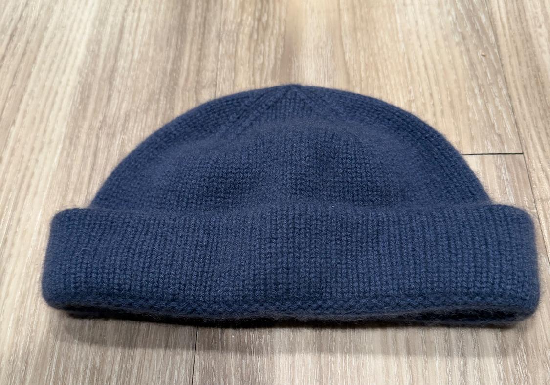 Navy knitted hat on a light wooden floor, showing soft texture and simple design with a folded brim.