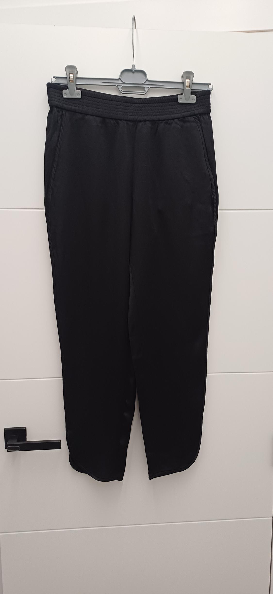 Black trousers hanging on a grey hanger over a white door. The fabric looks soft and has side pockets.