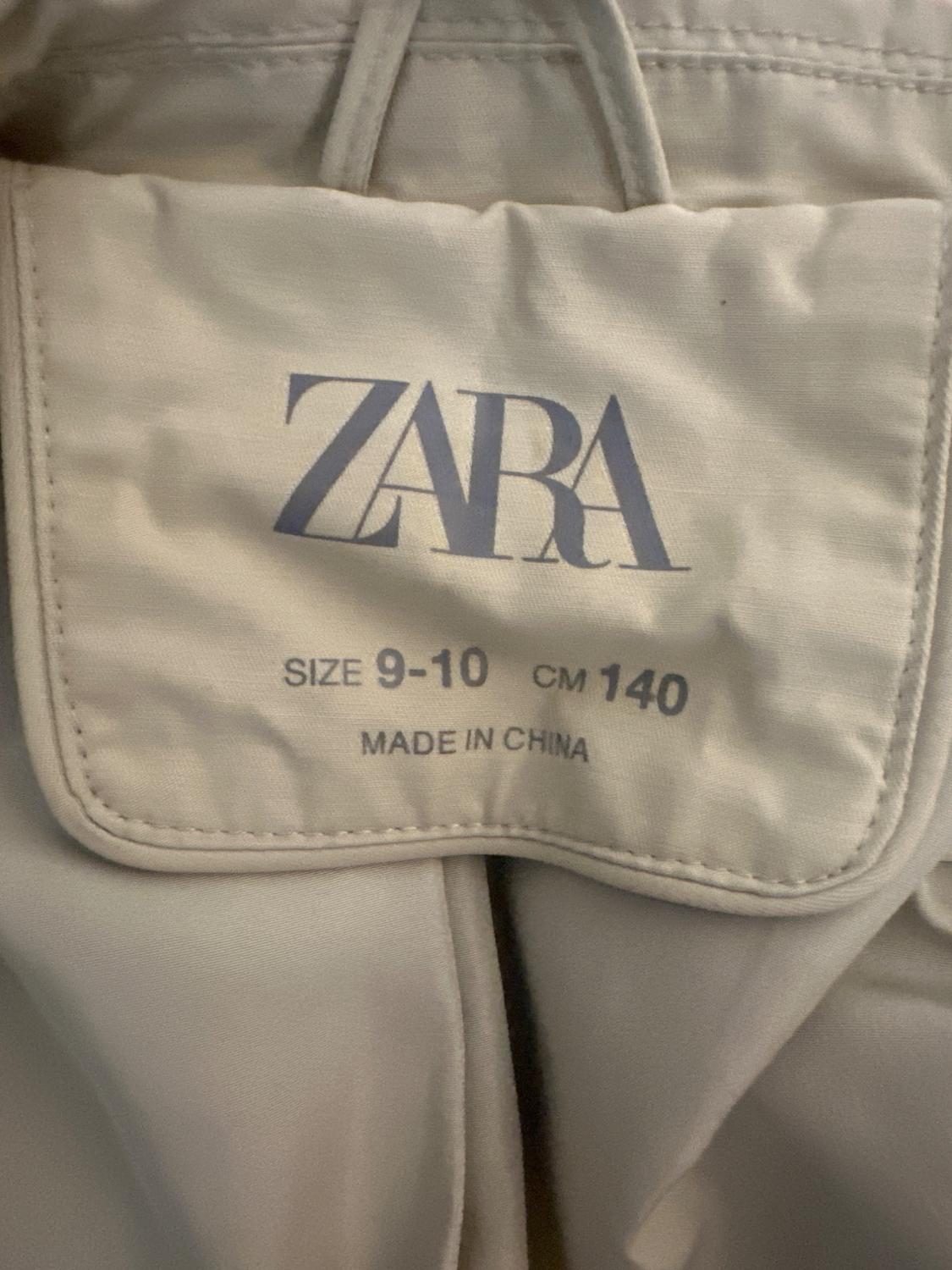 Close-up of a label on a beige garment with the text ZARA SIZE 9-10 CM 140 MADE IN CHINA.
