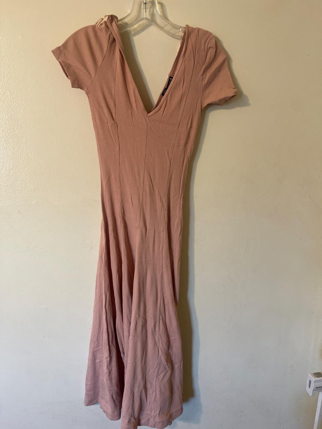 Light pink dress with a V-neckline and short sleeves, hanging on a clear hanger against a beige wall.