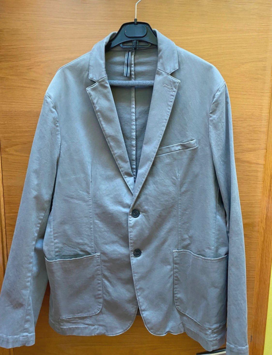 Light grey casual blazer with two buttons and front pockets, hanging on a black hanger against a wooden background.