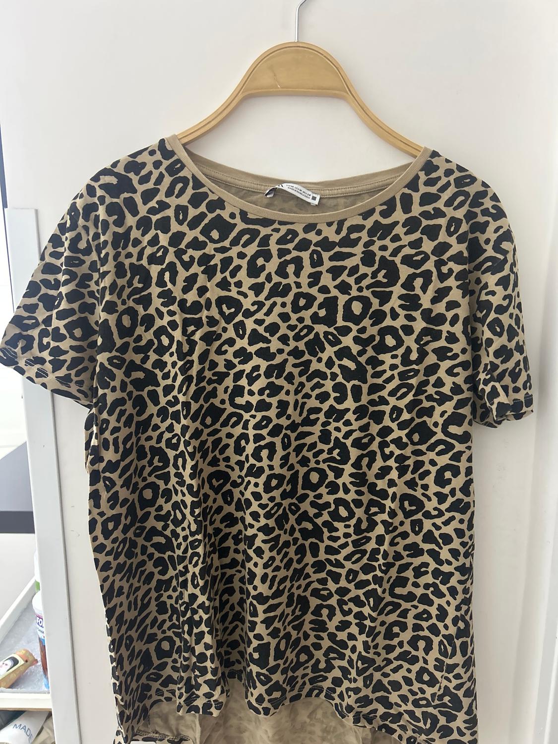 Short-sleeved T-shirt with a brown and black leopard print, hanging on a wooden hanger against a white background.