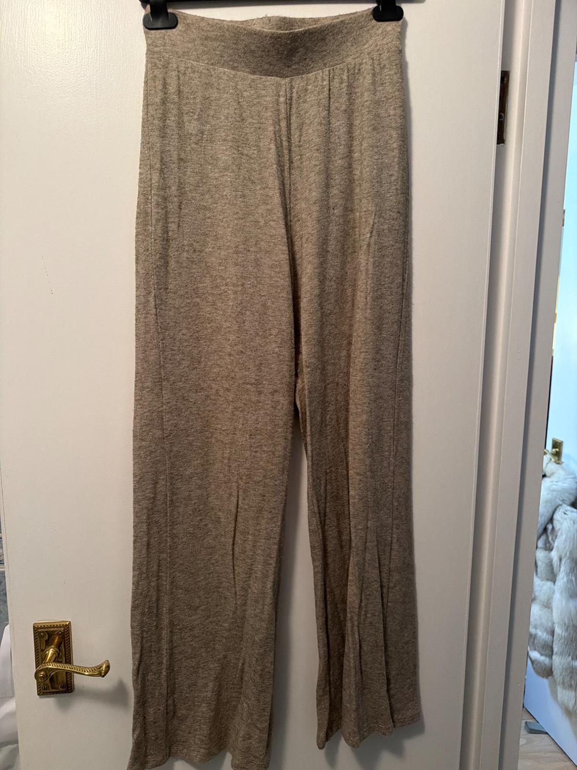 Grey soft fabric trousers hanging on a black hanger over a white door with a gold handle.