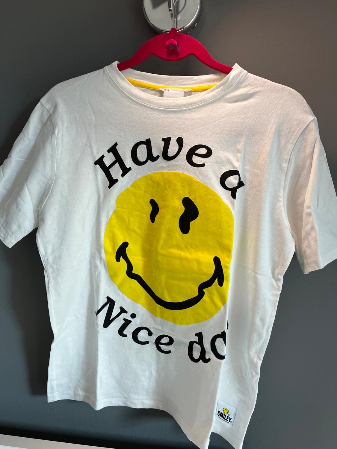 Front view of a white t-shirt with a yellow smiley face print and 'Have a Nice Day' text.