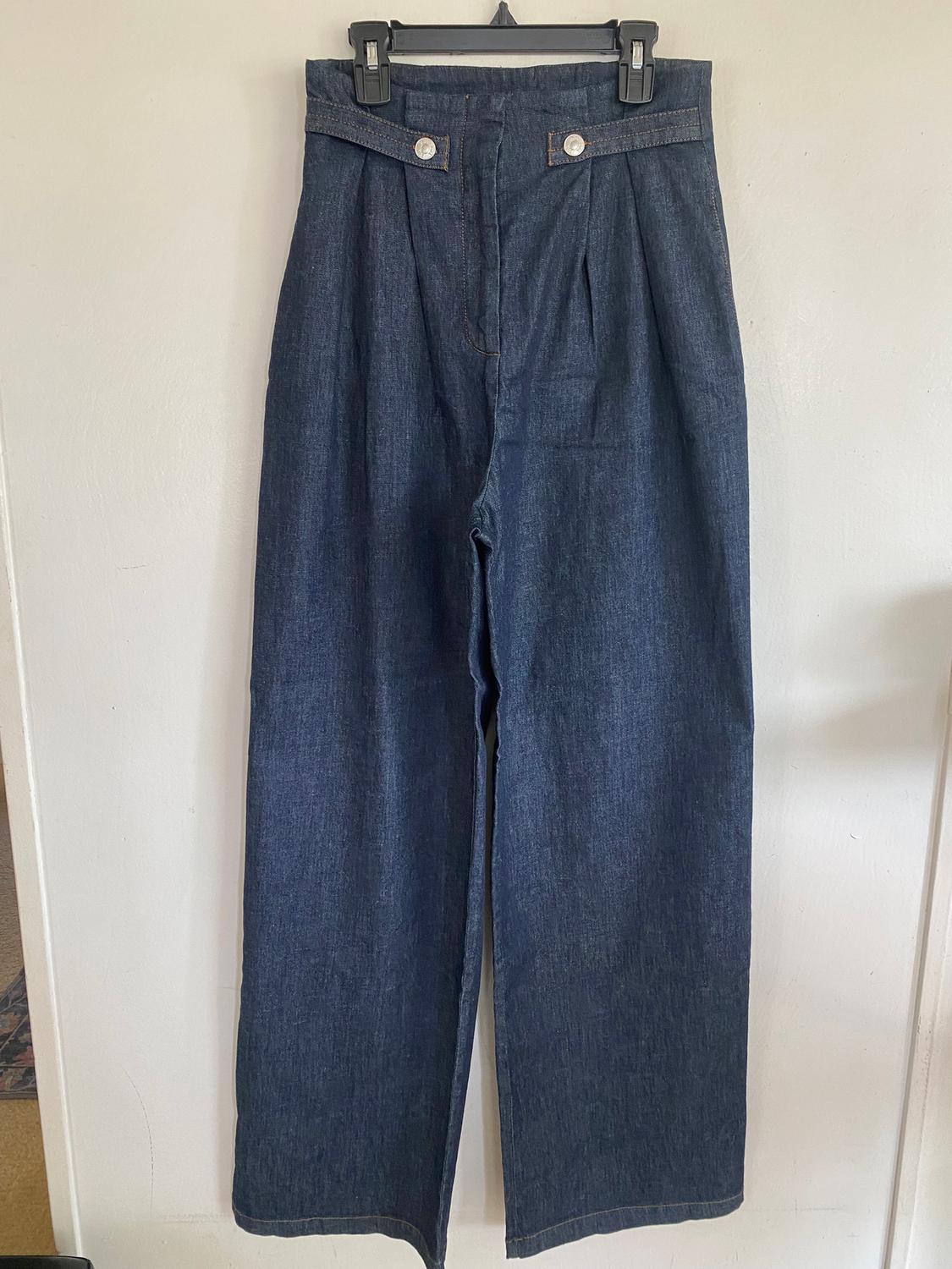 Dark blue denim pants hung on a black hanger, with silver buttons at the waist and pleats at the front.