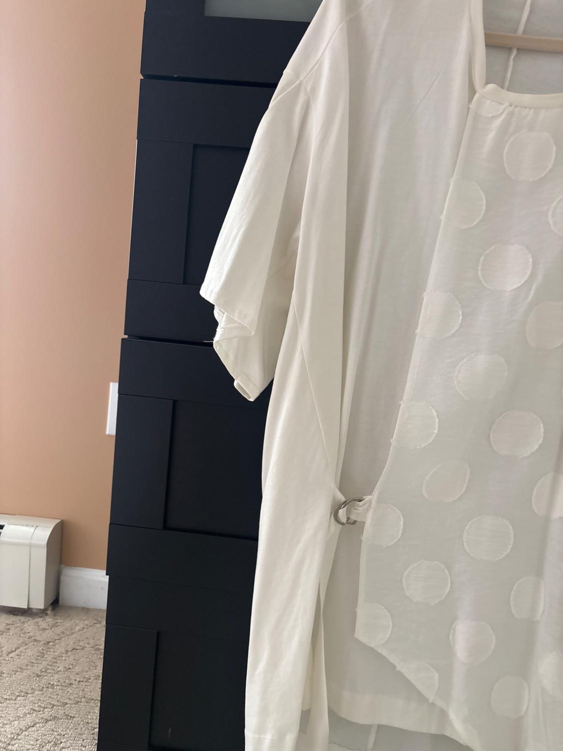 White shirt with a circle pattern hanging on a hanger, next to a black cabinet in a room with beige walls.