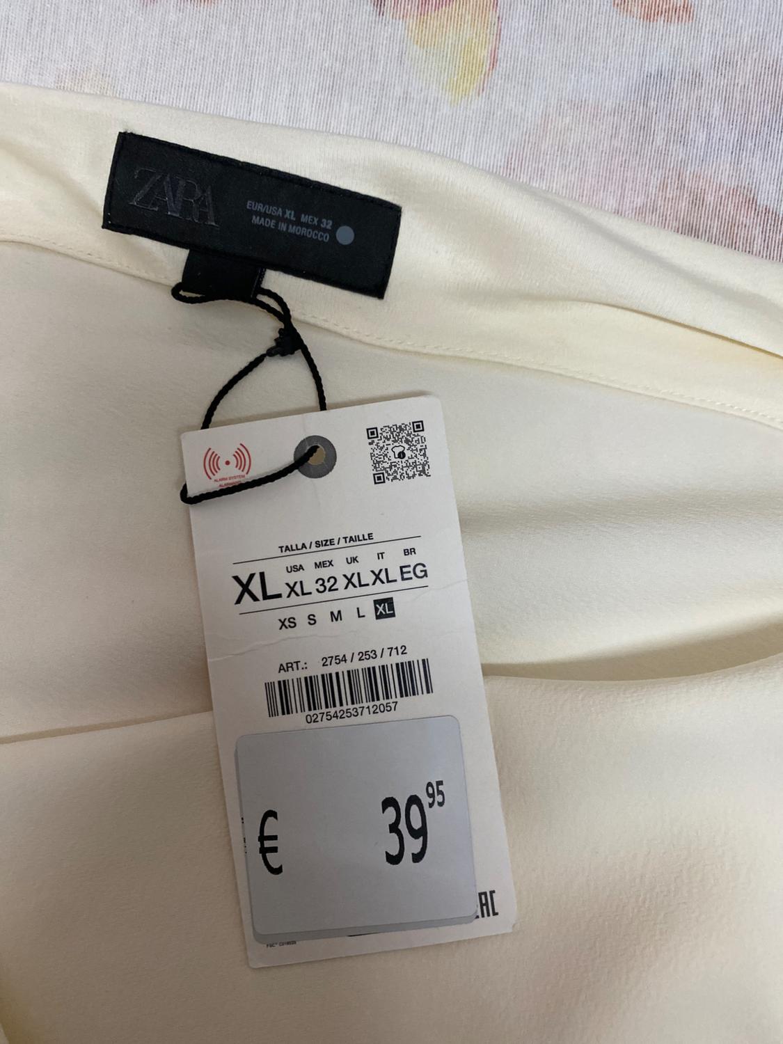 ZARA clothing label on white fabric, displaying size XL and price €39.95. Barcode and QR code visible. Made in Morocco.
