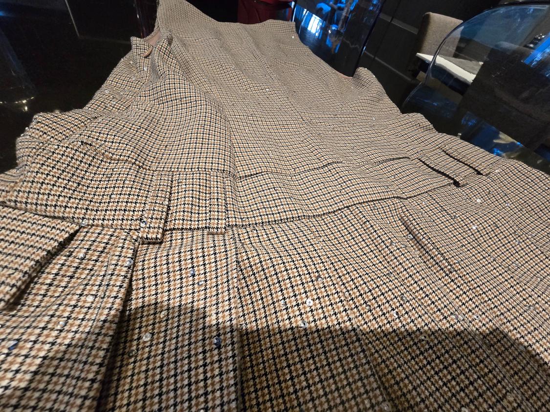 Fabric with a small plaid pattern in brown and black tones, spread over a dark surface in an indoor setting.