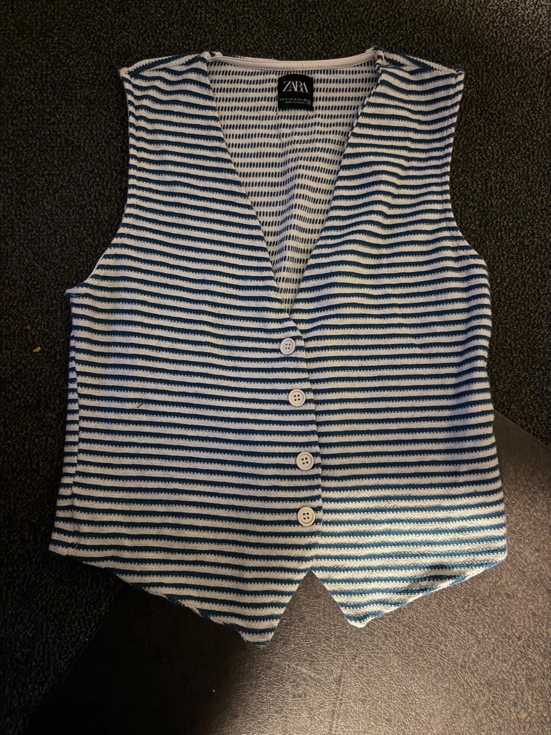 Blue and white striped vest with four white buttons, on a dark background. Visible label with text "ZARA".