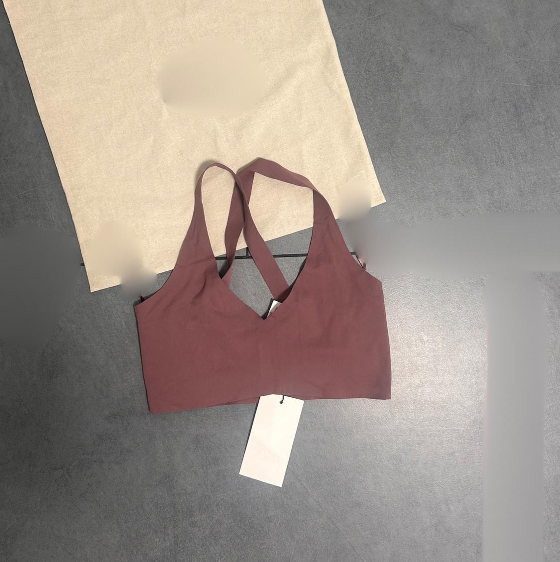Brown sports top with cross-back straps on a grey background and beige fabric. White tag hanging from the top.