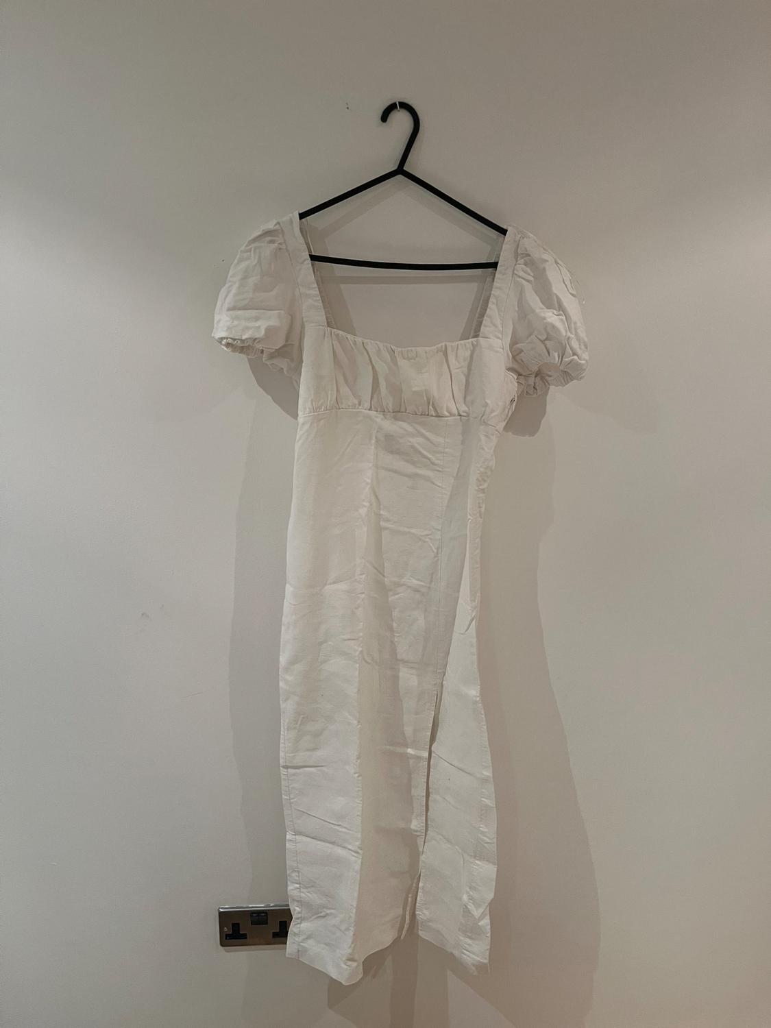 White dress with puff sleeves hanging on a black hanger against a white wall.