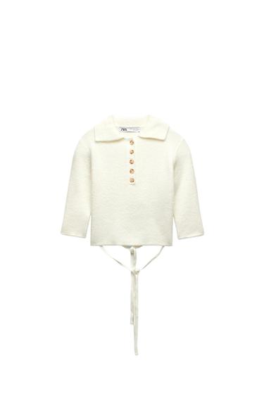 White sweater with a collar, brown buttons, and ties at the bottom. Visible "ZARA" tag. White background.