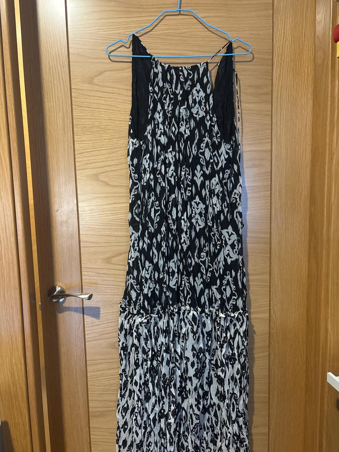 Long dress with a black and white abstract print, hanging on a blue hanger on a wooden door.