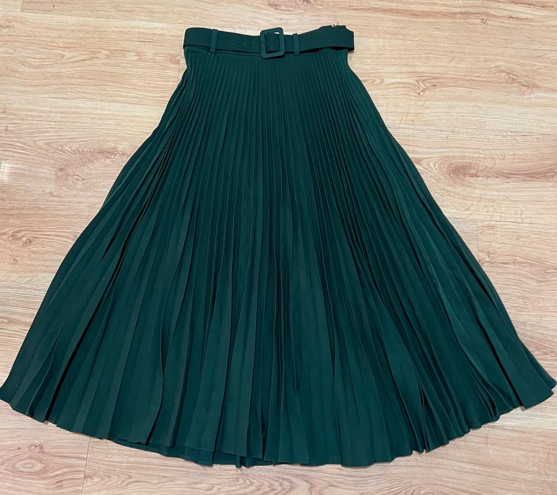 Dark green pleated skirt with a matching belt, laid out on a light wood floor.