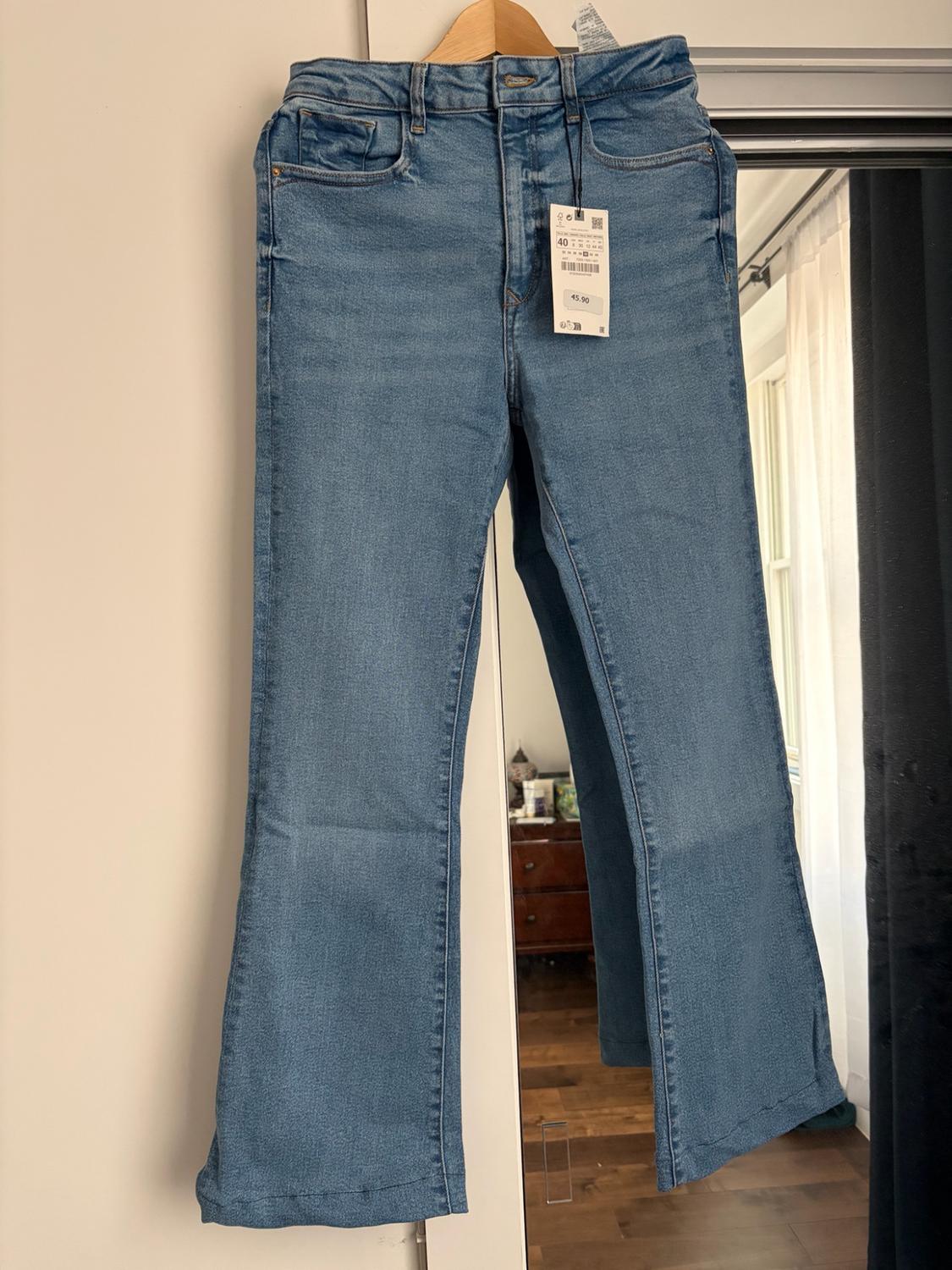 Blue jeans hanging on a hanger with a text label reading "40" and "45.90". To the right, a mirror reflects a room.