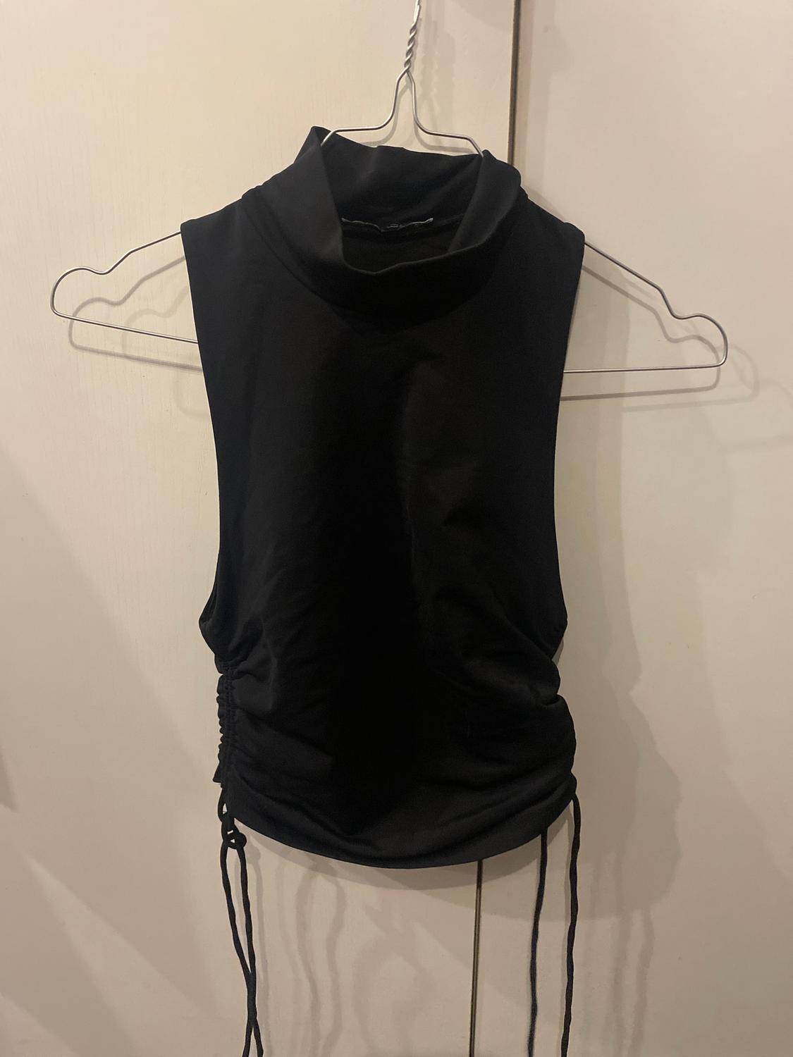 Black sleeveless high-neck top with side lacing, hanging on a wire hanger against a white background.