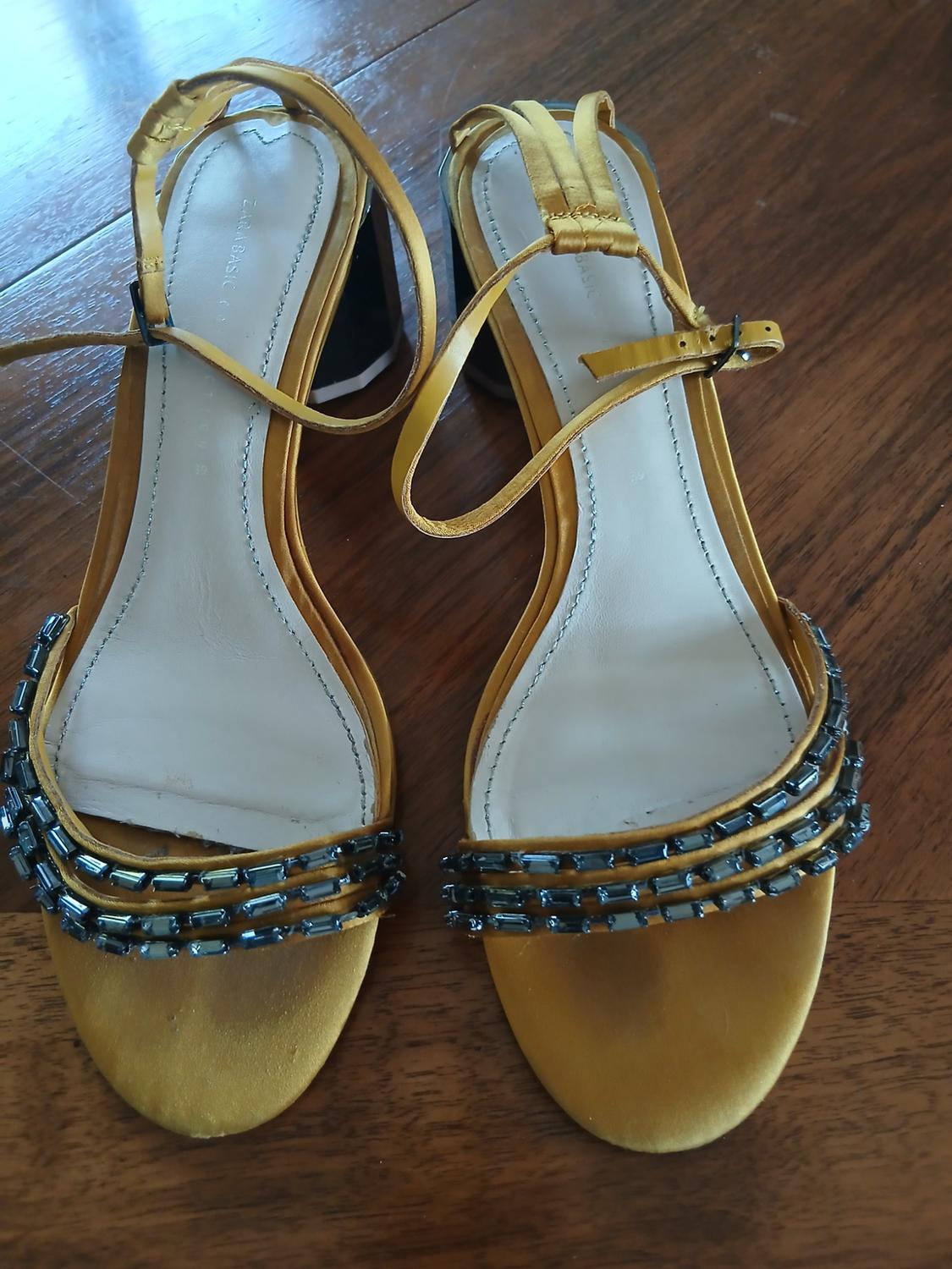 Detail of yellow heeled sandals with straps decorated with black beads.