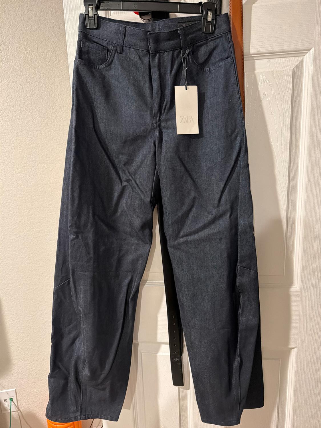 Dark blue trousers hanging on a black hanger with a Zara tag, over a white door.