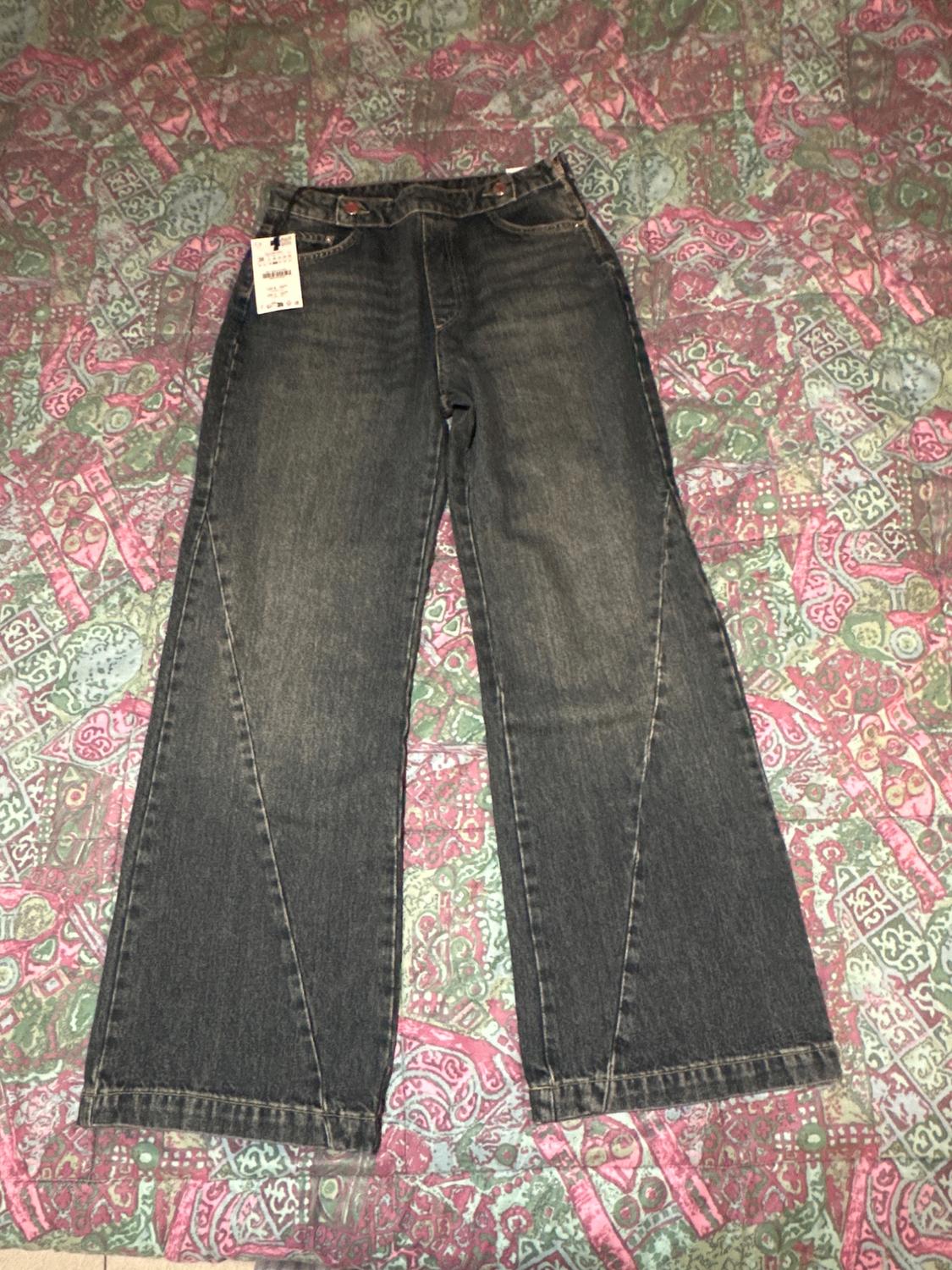 Dark wash, wide-leg jeans with a tag, on a pink, green, and blue patterned geometric quilt.