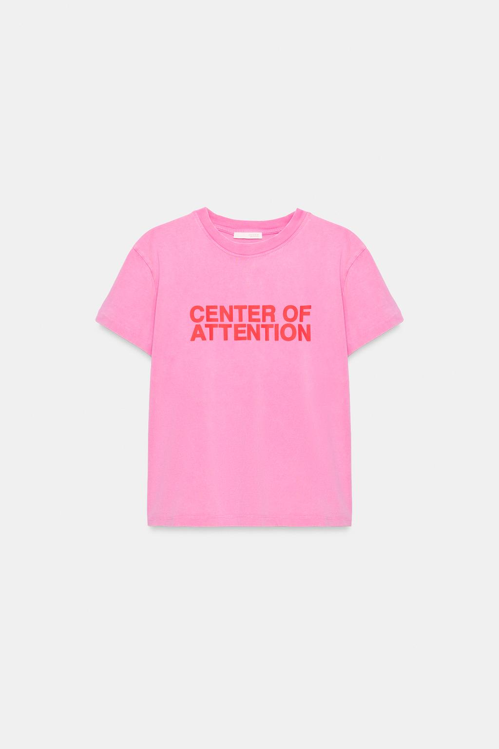 Front view of a short-sleeved, crew-neck pink t-shirt with the red text "CENTER OF ATTENTION" on the chest.