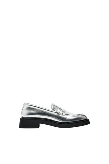 Silver loafer shoe with a black sole on a white background. Elegant and modern design, ideal for a sophisticated look.