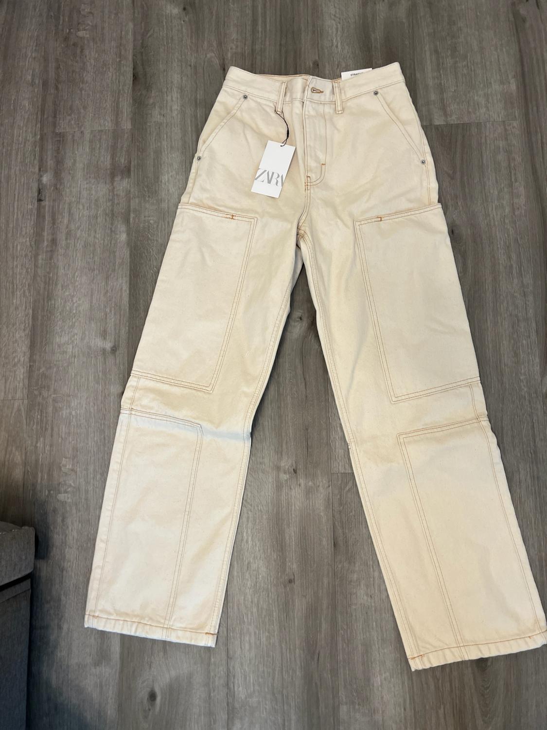 Beige straight-leg trousers with front patch pockets, laid out on a wooden floor. Label with the text ZARA.