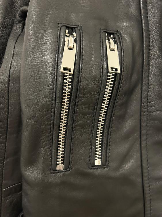 Detail of a black leather jacket with two silver metallic zips in the foreground.