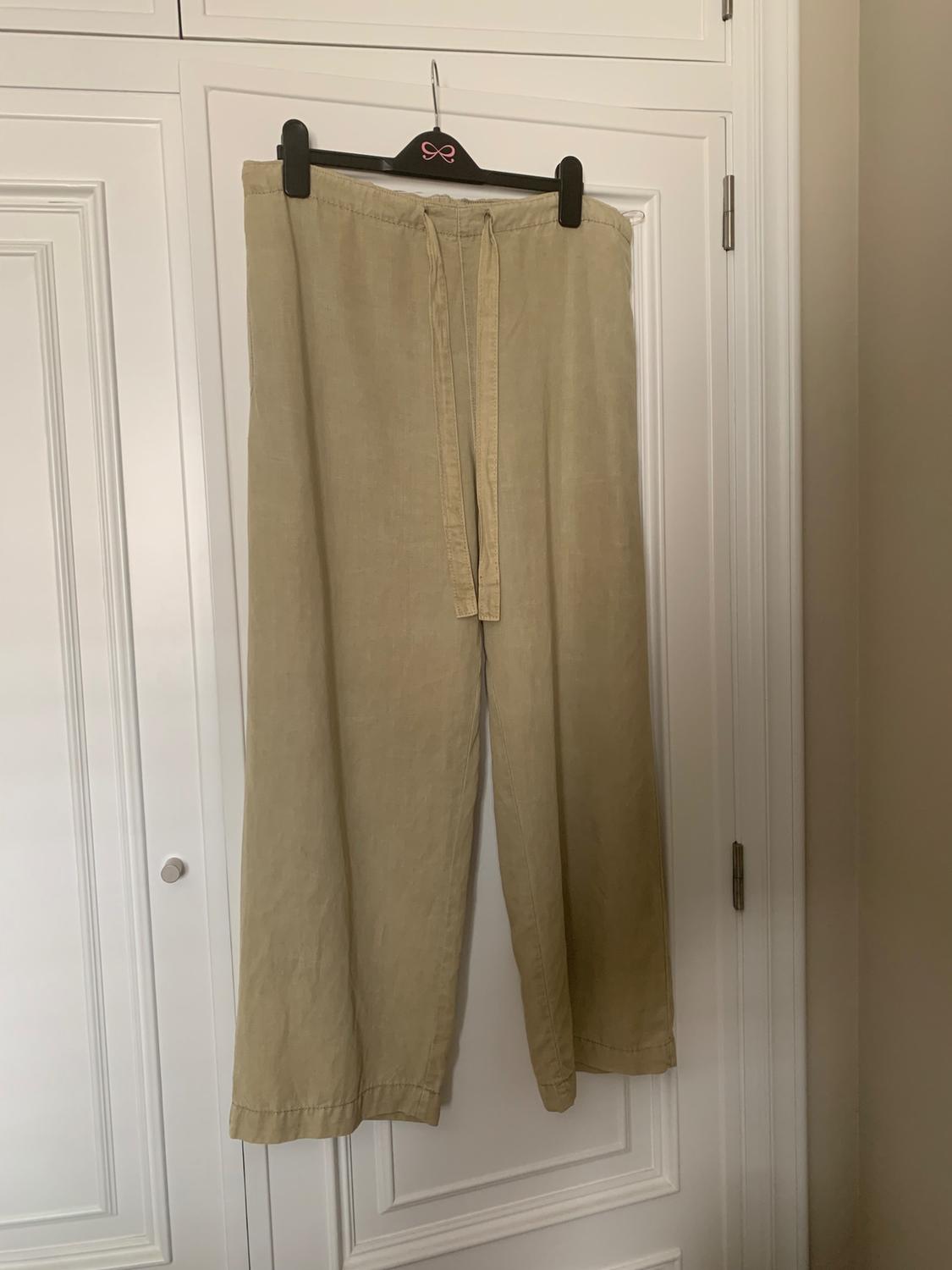 Beige linen trousers hanging on a black coat hanger with a pink bow, in front of a white wardrobe.