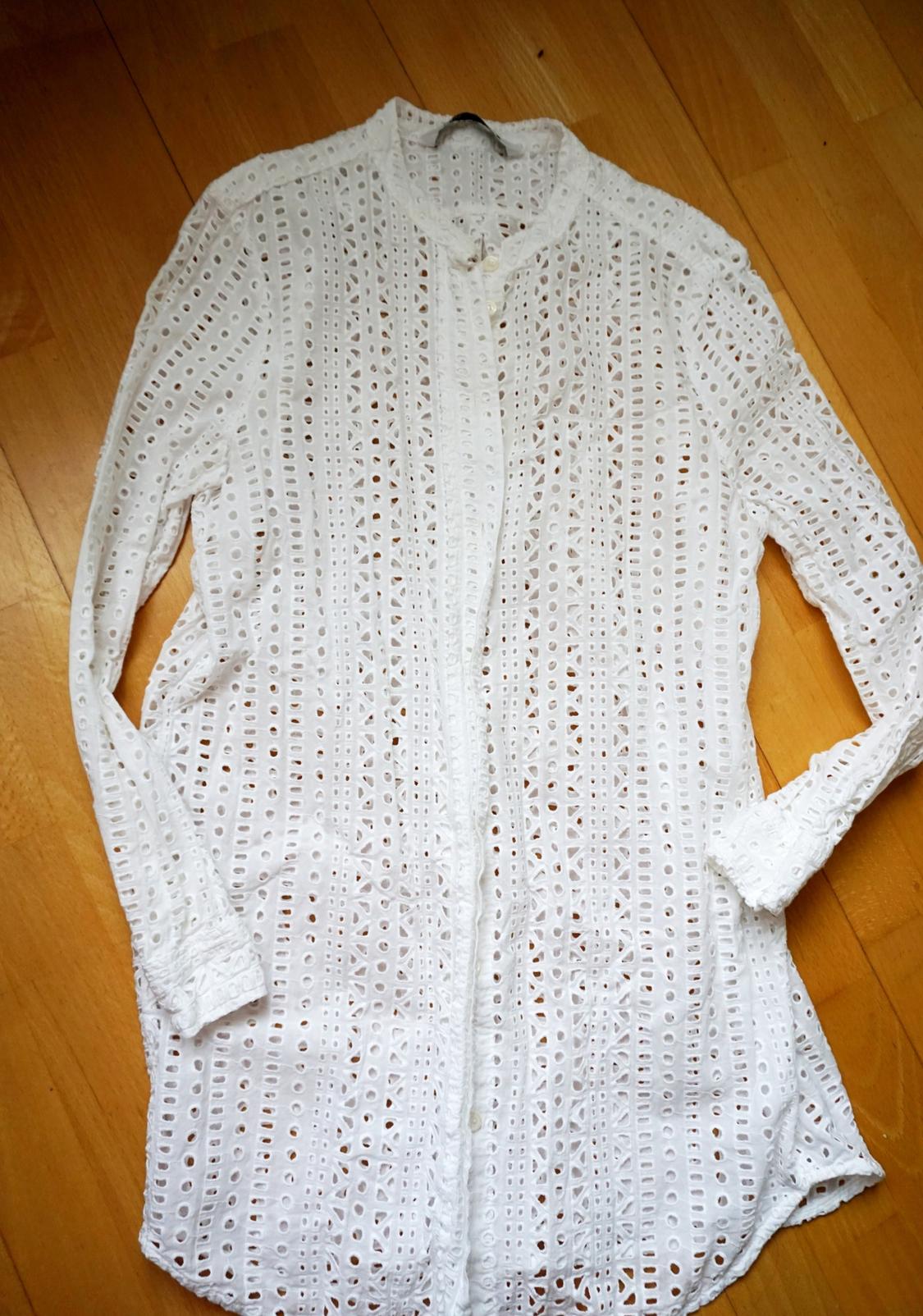 White long-sleeved lace shirt with an openwork pattern, on a light wooden floor.