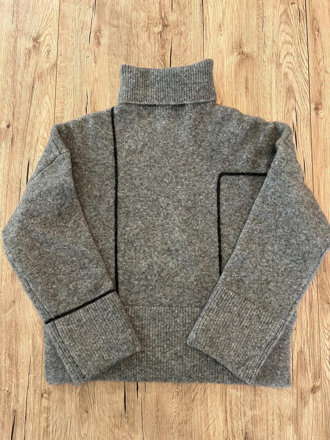 Grey knitted polo neck jumper with asymmetric black lines, on a wooden background. Relaxed composition in a warm and cosy style.