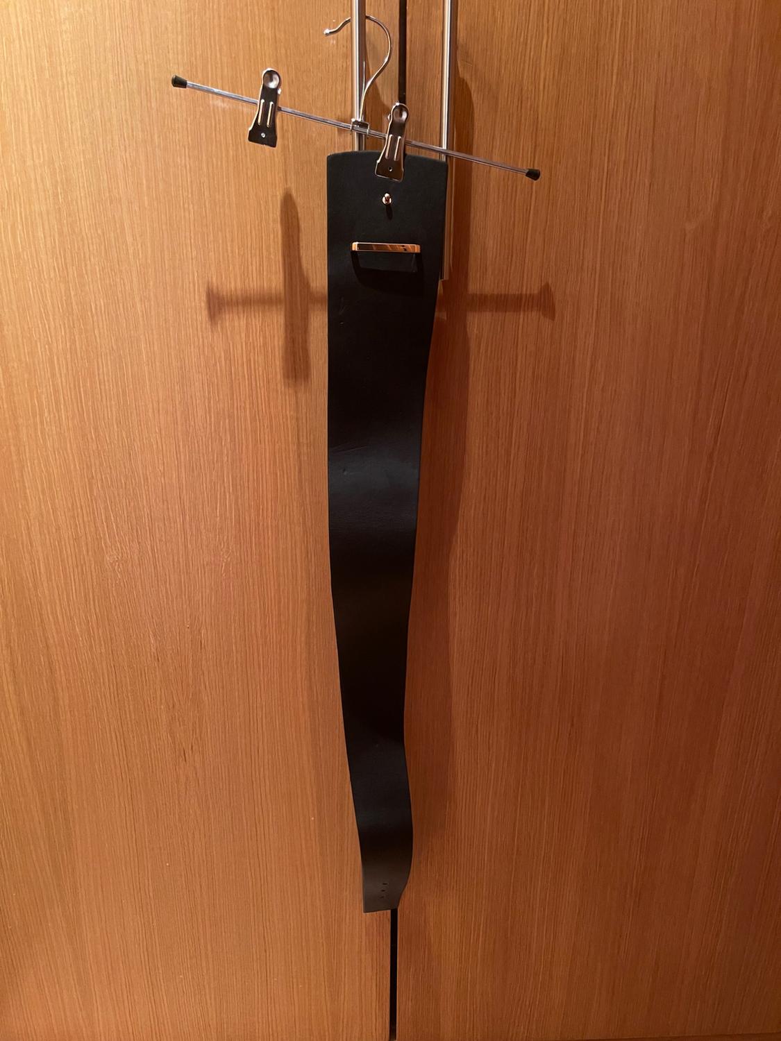Front view of a black belt hanging on a metal hanger.