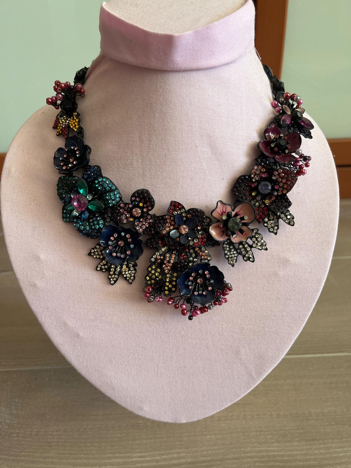 Floral necklace with colourful beads and sparkling stones on a pink fabric bust, on a light wooden surface.