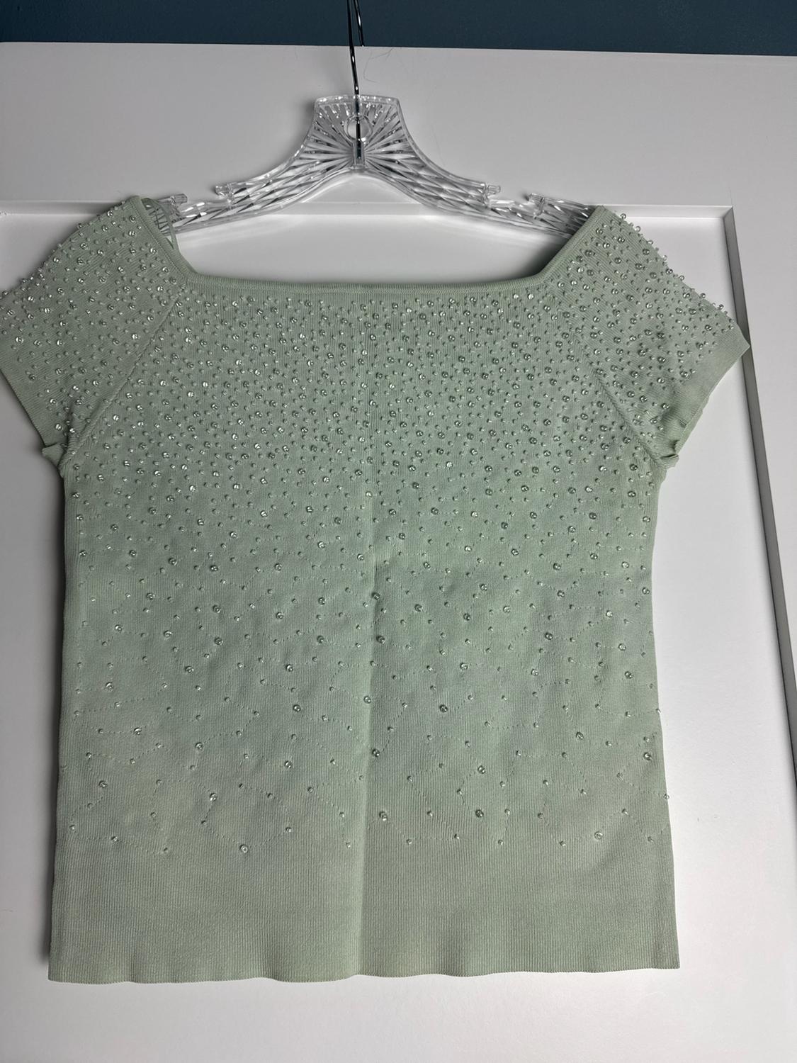 Light green short-sleeved knitted top with a square neckline, embellished with sparkly rhinestones, hanging on a transparent hanger.