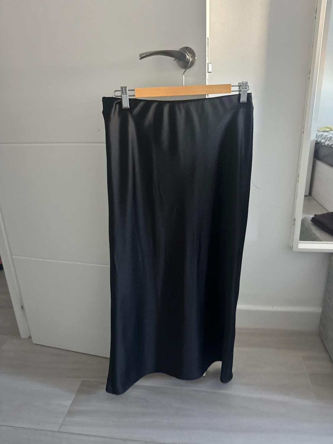 Black satin skirt hanging from a wooden hanger on the knob of a white door. Casual style in a relaxed setting.