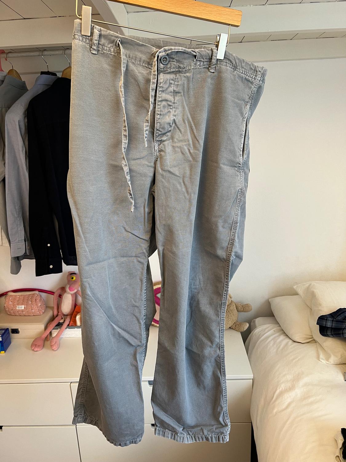 Grey trousers hanging on a wooden hanger in a bedroom, with toys and clothes in the background.