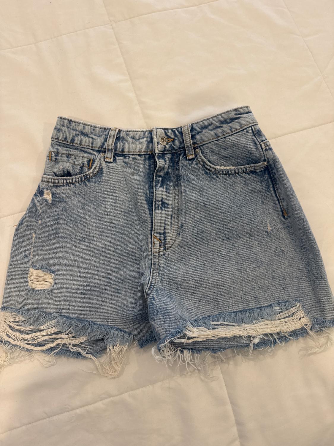 Light blue denim shorts with frayed edges and distressed details, on a white padded surface.