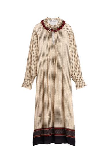 Front view of a long, printed dress with a ruffled and tied neckline, long puffed sleeves, and a dark detailed bottom hem.