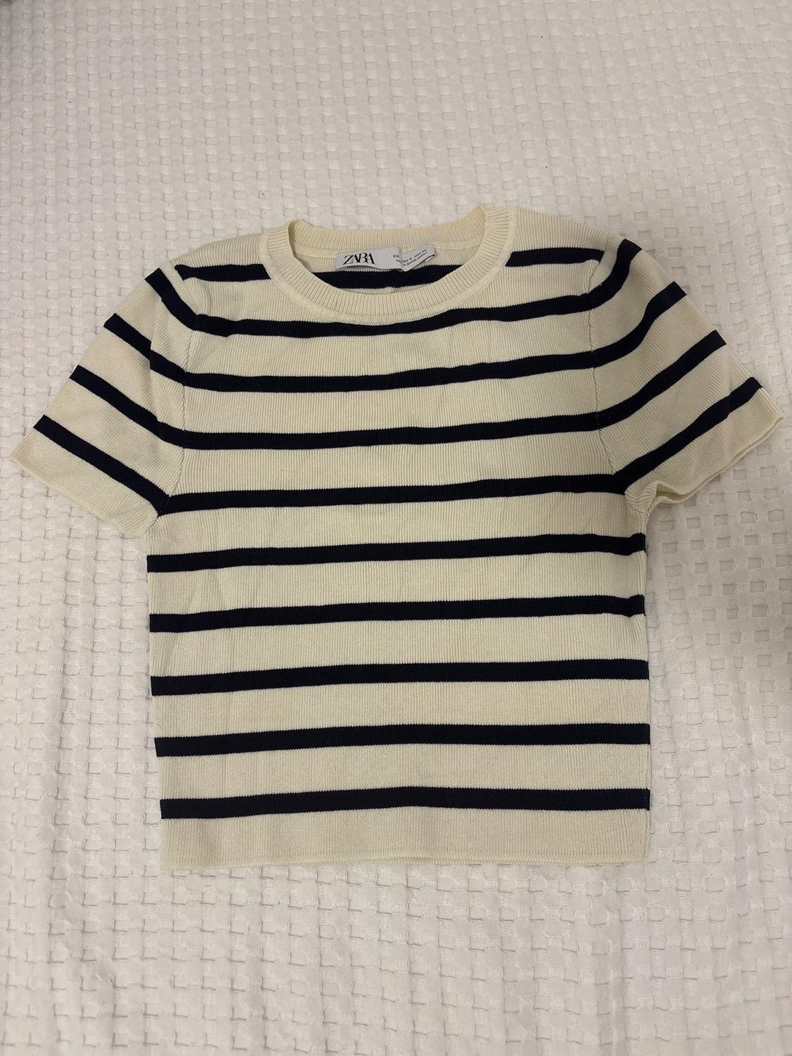 Black and cream horizontal striped T-shirt on a textured white surface. Visible label with the ZARA brand.