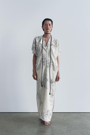 Souprava dlouhých bílých šatů s černým abstraktním potiskem, límcem s klopami, krátkými rukávy a předními kapsami.