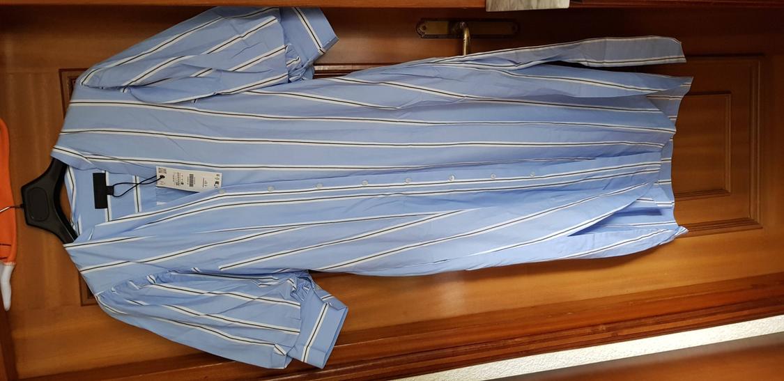 Blue shirt dress with white stripes and hang tag, hanging on a wooden door.