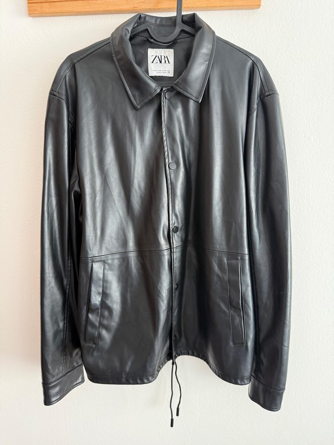 Black leather jacket hanging on a wooden hanger. Visible label with the text "ZARA". White background.