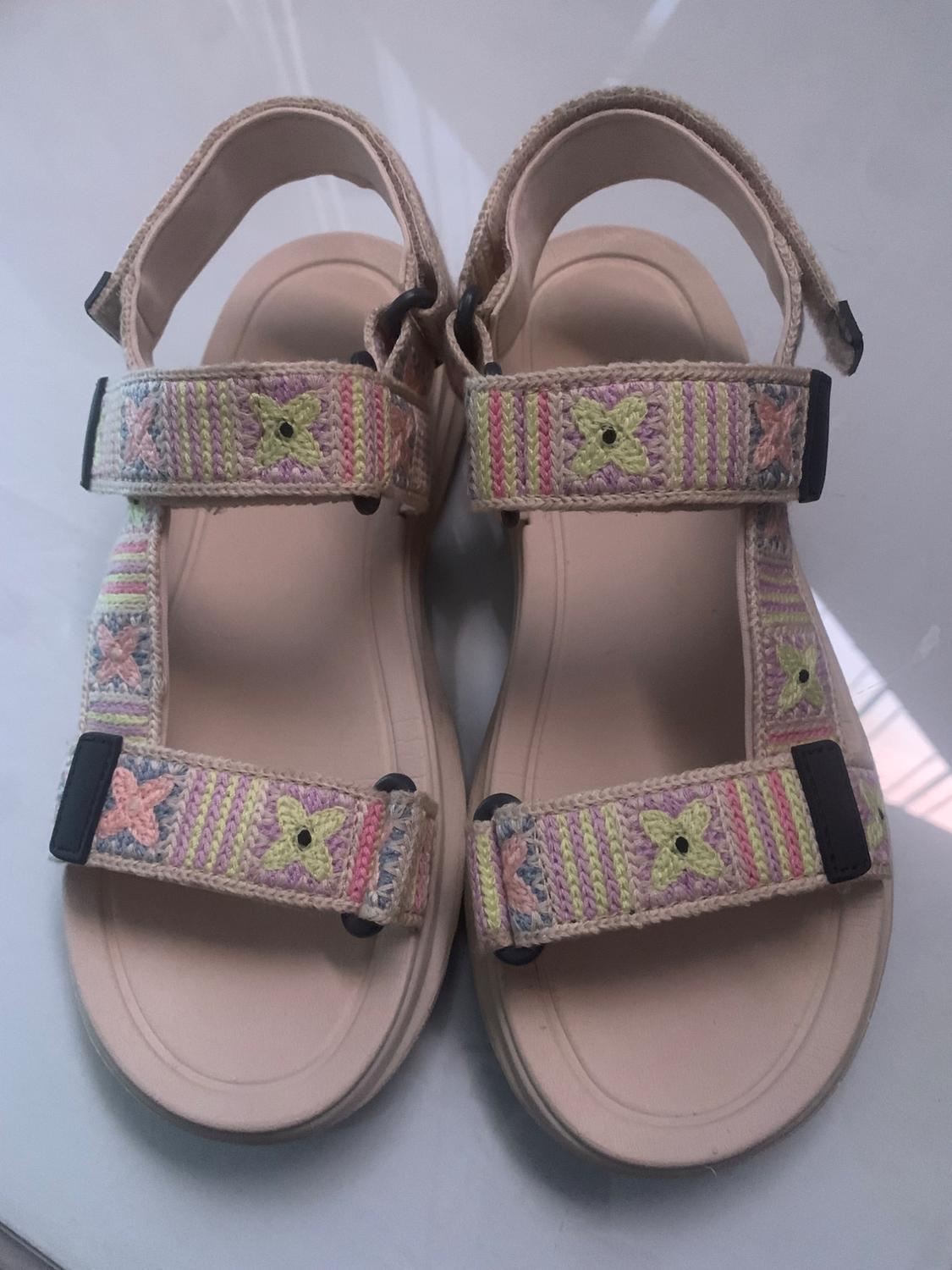 Front view of beige sandals with pastel-coloured embroidered straps and floral details.