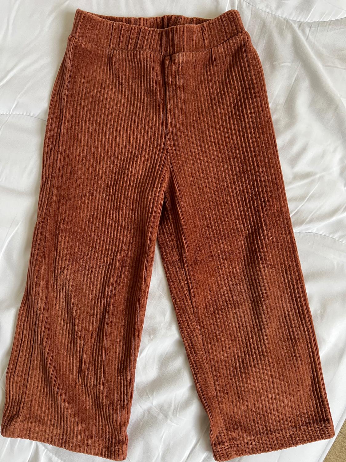 Brown ribbed corduroy trousers on a white surface, with an elasticated waist and a straight cut.