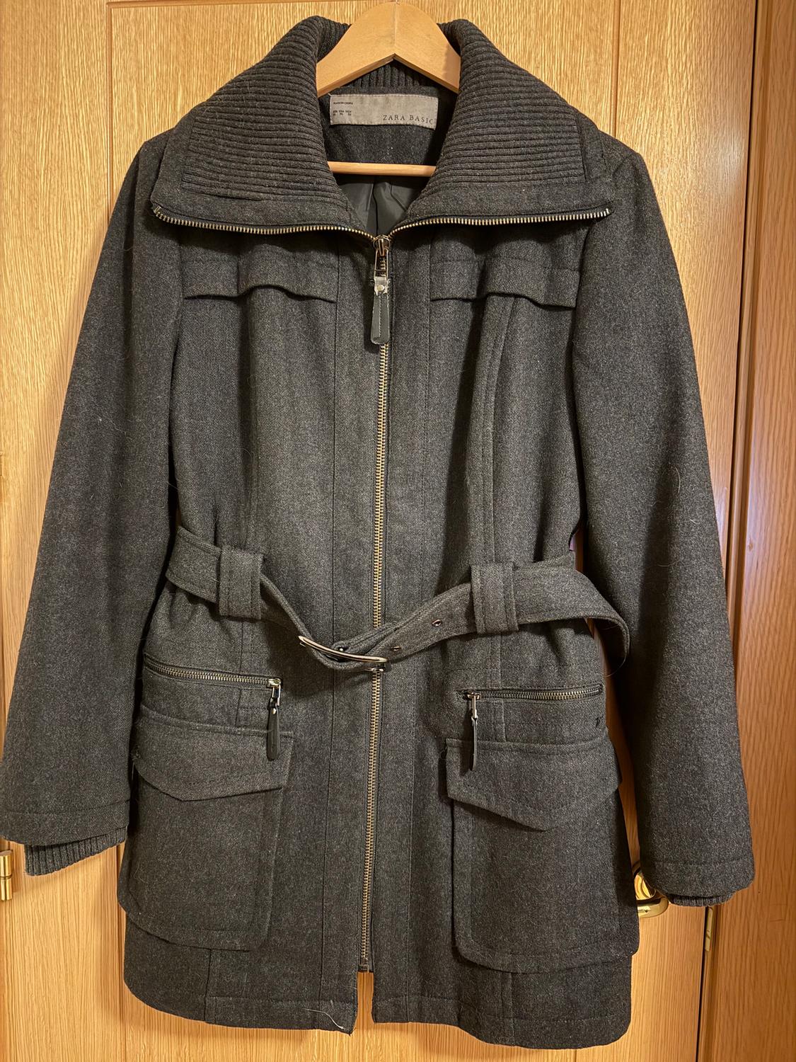 Dark grey coat with a zip and belt, hanging on a wooden hanger. Flap and zip pockets visible.